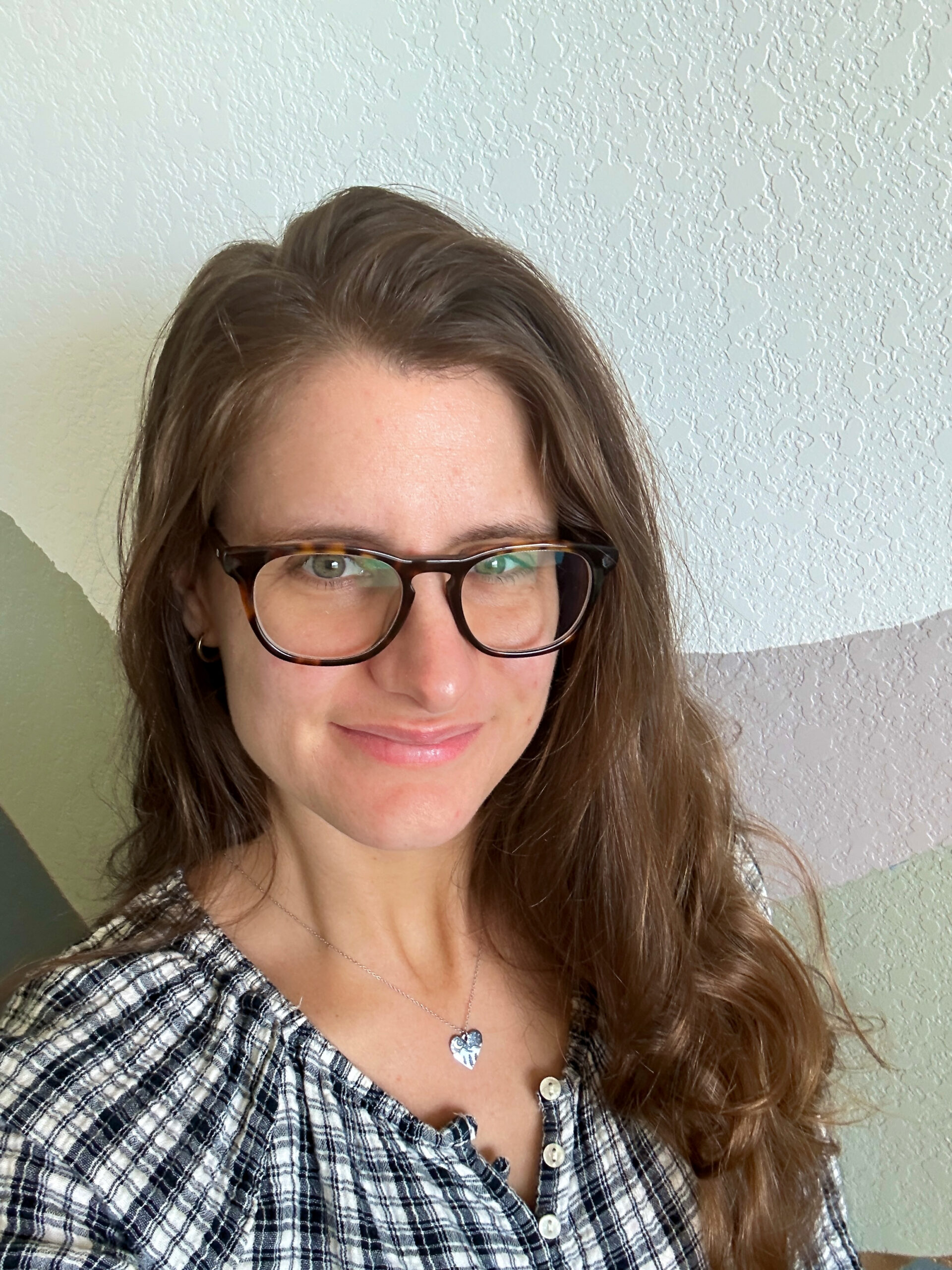 Portrait of Data Your Way Founder Stefani Harrison with tortoise shell colored round glasses and long wavy brown hair wearing a plaid patterned black and white shirt with a heart shaped necklace and tiny hooped earnings.